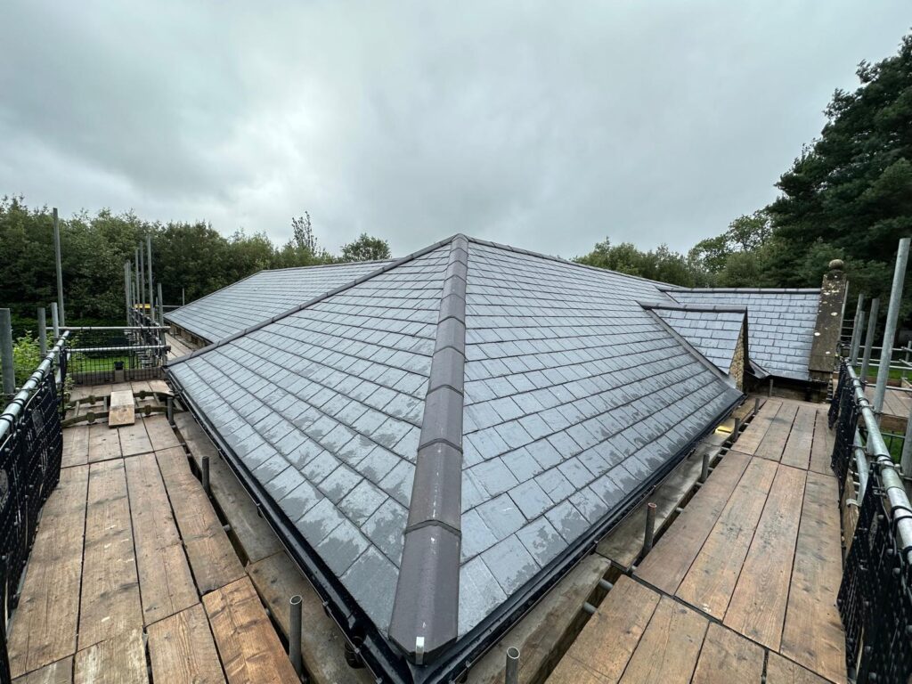 A roof with beautiful slating, completed it Oxfordshire. There is a greyish sky in the background.
