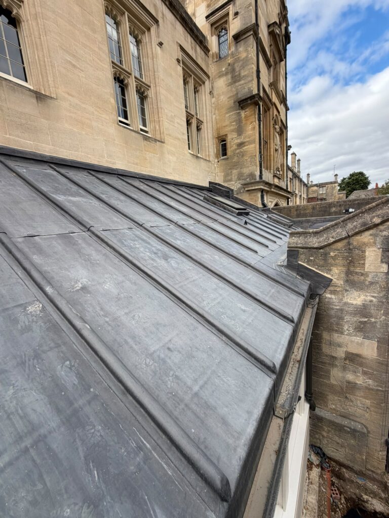 Completed Code 8 milled lead roof on the new Deanery extension at Christ Church, Oxford, with wood-cored rolls running down the slope and the college’s Gothic stonework rising behind.